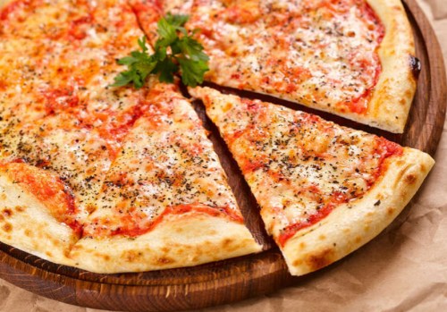 A freshly baked cheese pizza with a slice cut out, garnished with herbs, on a wooden serving board.