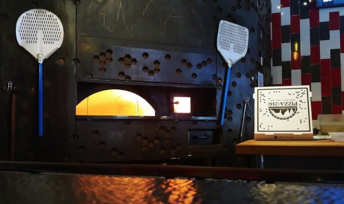 A pizza oven with a glowing opening, flanked by pizza peels, set in a colorful restaurant interior.