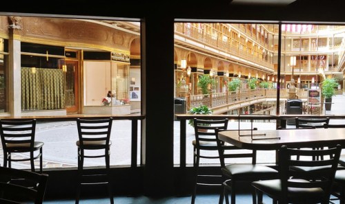 View of an indoor atrium with shops and greenery, seen through large windows from a seating area.