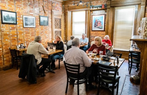 A cozy restaurant with brick walls, featuring diners at wooden tables enjoying meals and drinks.
