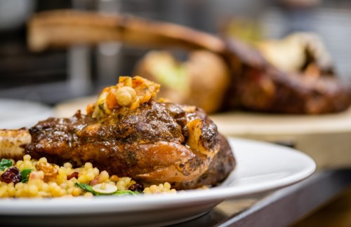 A beautifully plated lamb chop with couscous and garnishes, set in a restaurant kitchen.