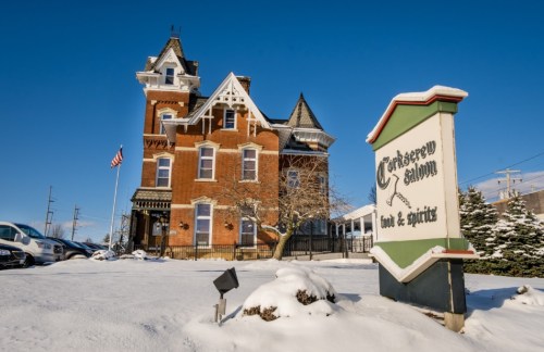 Historic building with a tower, snow-covered ground, and a sign for "Cranberry Saloon" under a clear blue sky.