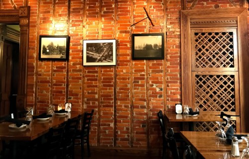 Cozy restaurant interior with exposed brick walls, wooden tables, and vintage photos hanging above.