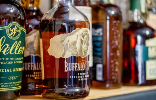 A close-up of whiskey bottles on a shelf, featuring a prominent Buffalo Trace bourbon bottle.