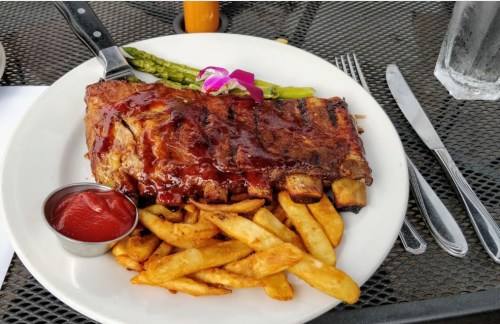 A plate of barbecue ribs with sauce, served with fries and asparagus, garnished with a purple flower.
