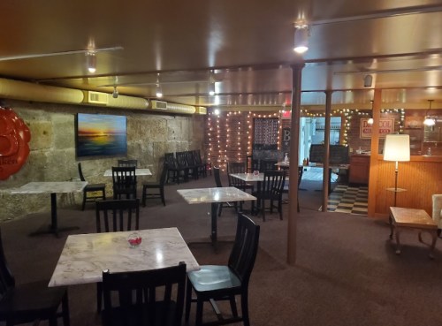 Cozy restaurant interior with marble tables, black chairs, and warm lighting, featuring stone walls and decorative accents.