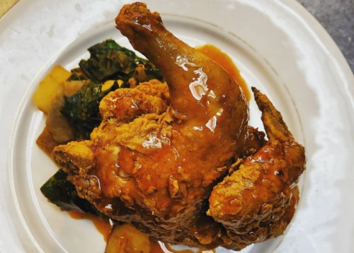 A plate featuring a crispy fried chicken leg with a glossy sauce, served alongside sautéed greens and vegetables.