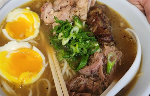 A bowl of ramen with soft-boiled eggs, green onions, and various meats in a rich broth.