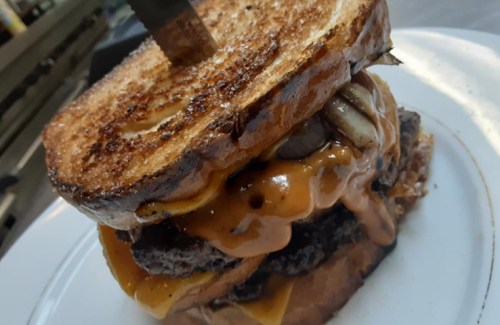 A towering burger with melted cheese and peanut butter, sandwiched between two slices of toasted bread.