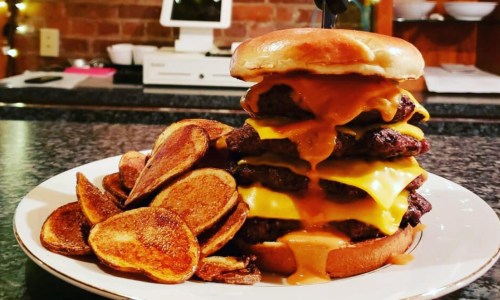 A towering burger with multiple beef patties, melted cheese, and a side of crispy potato chips on a plate.