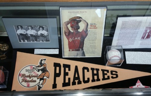 Display case featuring a vintage baseball pennant, a newspaper article, and memorabilia related to the Rockford Peaches.