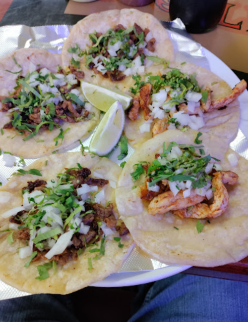 A plate of five tacos filled with meat, onions, and cilantro, garnished with lime wedges.
