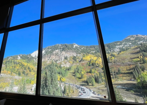 A scenic view of mountains and trees with autumn colors, framed by large windows under a clear blue sky.