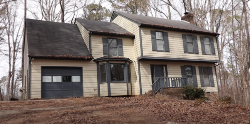 A two-story yellow house with a garage, surrounded by bare trees and fallen leaves.