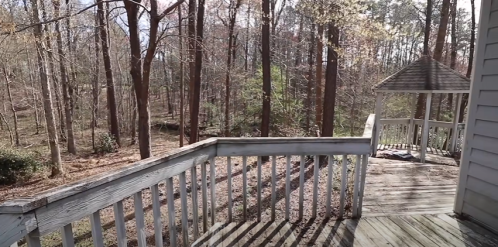 A wooden deck overlooks a wooded area with trees and a gazebo in the background, showcasing a serene outdoor setting.