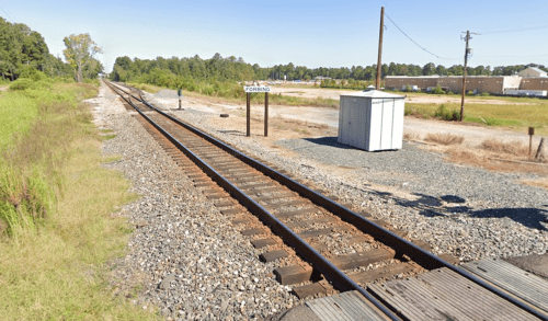 A view of railway tracks stretching into the distance, with a small shelter and a sign labeled "CORSO."