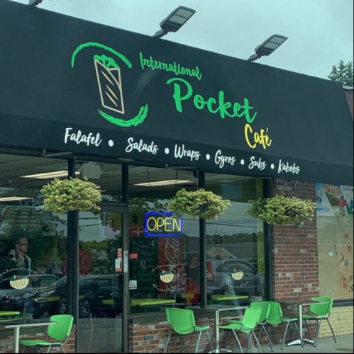 Exterior of International Pocket Café featuring a sign and open door, with green chairs outside and a menu of Mediterranean dishes.