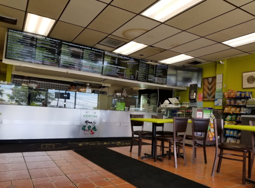 Interior of a casual eatery with a menu board, counter, and seating area, featuring green accents and snacks for sale.