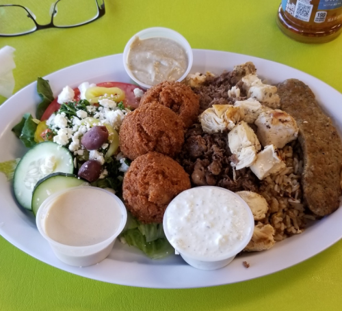 A colorful plate featuring rice, grilled chicken, falafel, salad, and two dipping sauces on a bright green table.