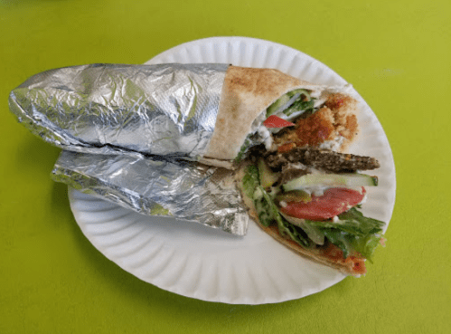 A partially unwrapped wrap filled with vegetables and crispy ingredients on a paper plate, set against a green background.