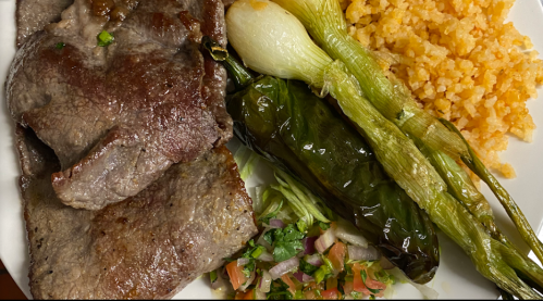 A plate featuring grilled meat, rice, grilled green onions, a stuffed pepper, and a fresh salad with tomatoes and herbs.