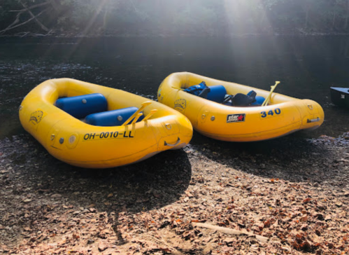 Two yellow inflatable rafts are moored on a riverbank, surrounded by trees and sunlight filtering through.