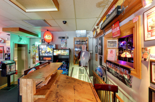 A cozy bar interior featuring a wooden counter, colorful lights, and various decorations on the walls.
