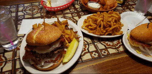 A hearty burger with bacon and cheese, served with fries and a side of curly fries, alongside a glass of water.