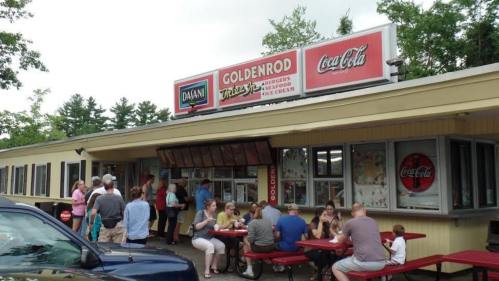 A busy ice cream shop with outdoor seating, people enjoying treats, and a sign for Goldenrod and Coca-Cola.