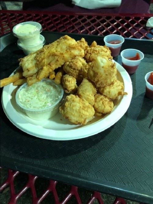 A plate of fried fish and chicken, served with fries, coleslaw, and dipping sauces in small cups.
