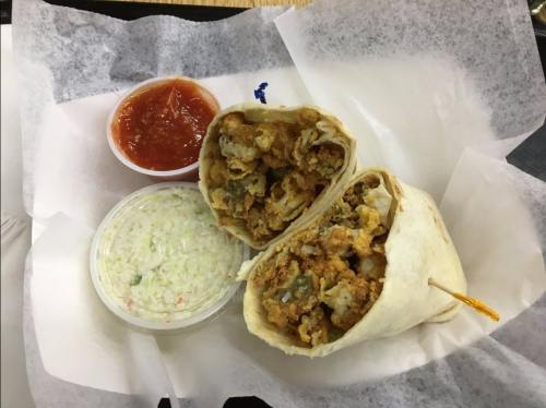 A cut burrito filled with fried ingredients, served with salsa and coleslaw on the side, in a takeout container.