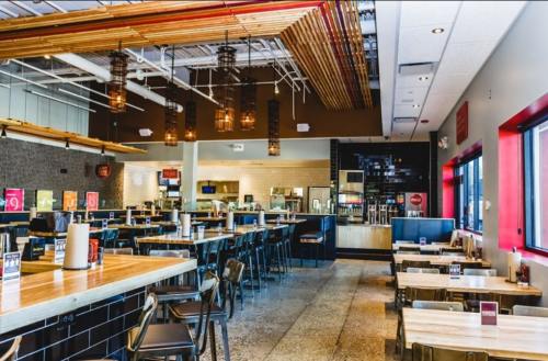Modern restaurant interior with wooden accents, pendant lights, and empty tables arranged for dining.