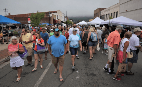 A bustling street fair with crowds of people walking among vendor tents under a cloudy sky.