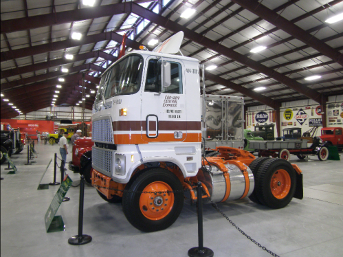 A vintage truck displayed in a museum, featuring a white and orange color scheme and classic design elements.