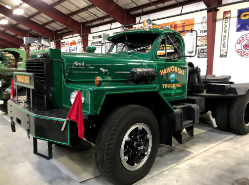 A vintage green Mack truck with "Yaworski Trucking" signage, displayed indoors with a shiny chrome grille and black wheels.