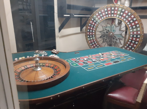 A casino table with a roulette wheel and betting layout, featuring chips and a green felt surface.