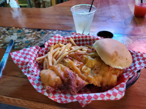 A basket of fried chicken with cheese, fries, and a bun, alongside a glass of lemonade on a wooden table.