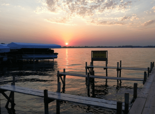 Sunset over a calm lake, with silhouetted docks and a sign, creating a serene and picturesque scene.