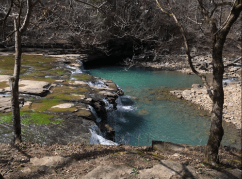 A serene natural scene featuring a turquoise pool surrounded by rocky terrain and bare trees.