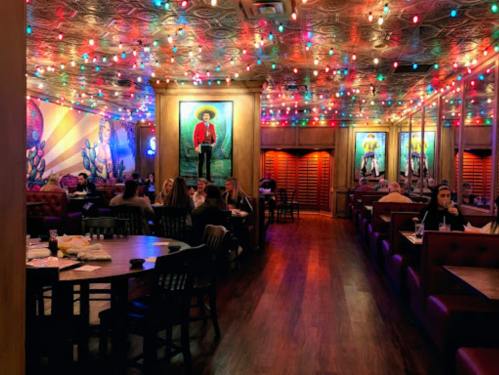 A vibrant restaurant interior with colorful lights, wooden tables, and artwork on the walls, filled with diners.