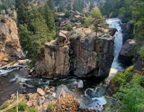 A scenic view of a waterfall cascading over rocky cliffs, surrounded by lush greenery and trees.