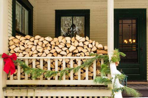 A porch decorated for the holidays, featuring a stacked pile of firewood and festive greenery with a red bow.