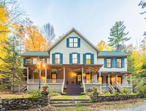 A charming two-story house with green shutters, surrounded by autumn trees and warm evening lights.