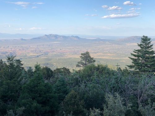 A panoramic view of mountains and valleys under a clear sky, surrounded by lush greenery.