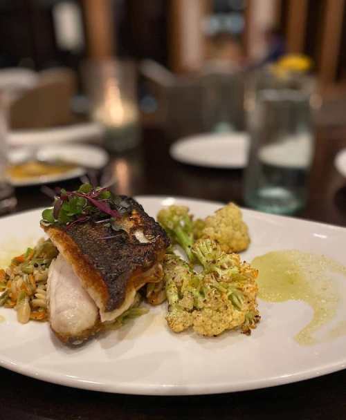 A plated dish featuring crispy fish, roasted cauliflower, and a colorful vegetable medley, elegantly arranged.