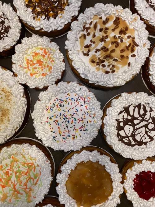 A variety of decorated mini pies topped with whipped cream and colorful sprinkles, arranged on a tray.