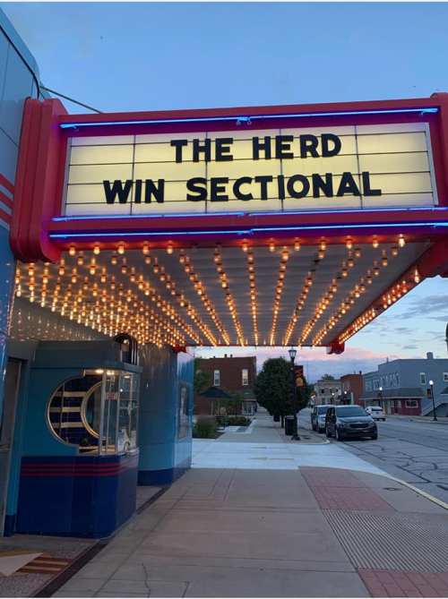 Marquee of a theater displaying "THE HERD" and "WIN SECTIONAL" with bright lights and a blue exterior.