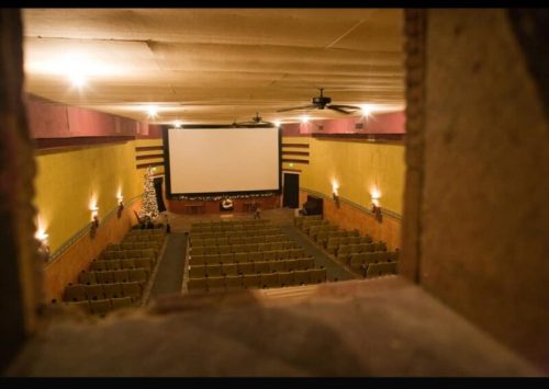 View of an empty theater from a balcony, featuring rows of green seats and a large screen at the front.