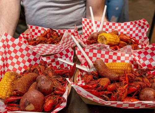 Four baskets of spicy crawfish, potatoes, corn, and sausage on a table, lined with red and white checkered paper.