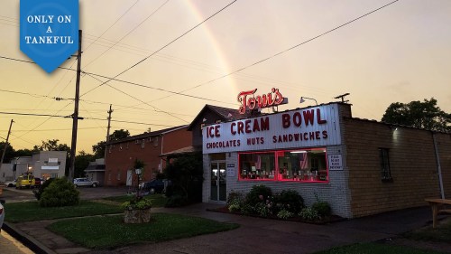 A quaint ice cream shop with a rainbow in the background, featuring a sign that reads "Tom's Ice Cream Bowl."